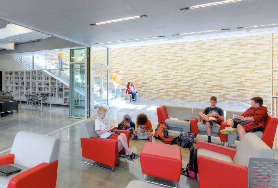 Students learning in a bright space with red seating and a textured masonry wall