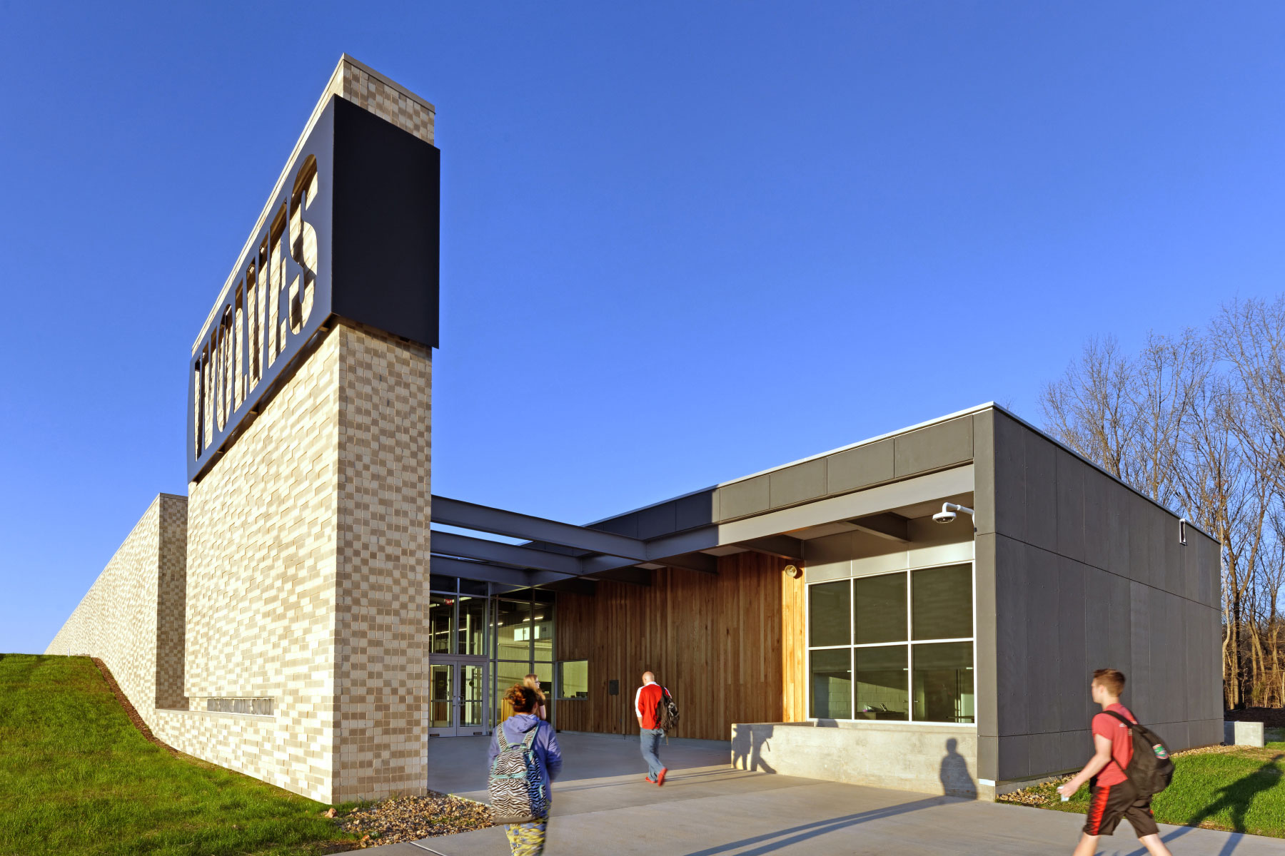 Students approaching a school entrance with a tall masonry sign and sheltered entryway